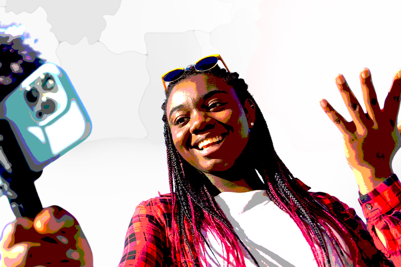Smiling young woman taking a selfie, wearing a red plaid shirt and sunglasses on her head, waving at the camera.